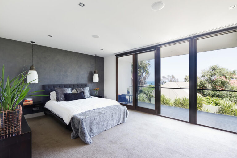 A cozy bedroom with large sliding glass doors, allowing natural light to fill the space through the windows.